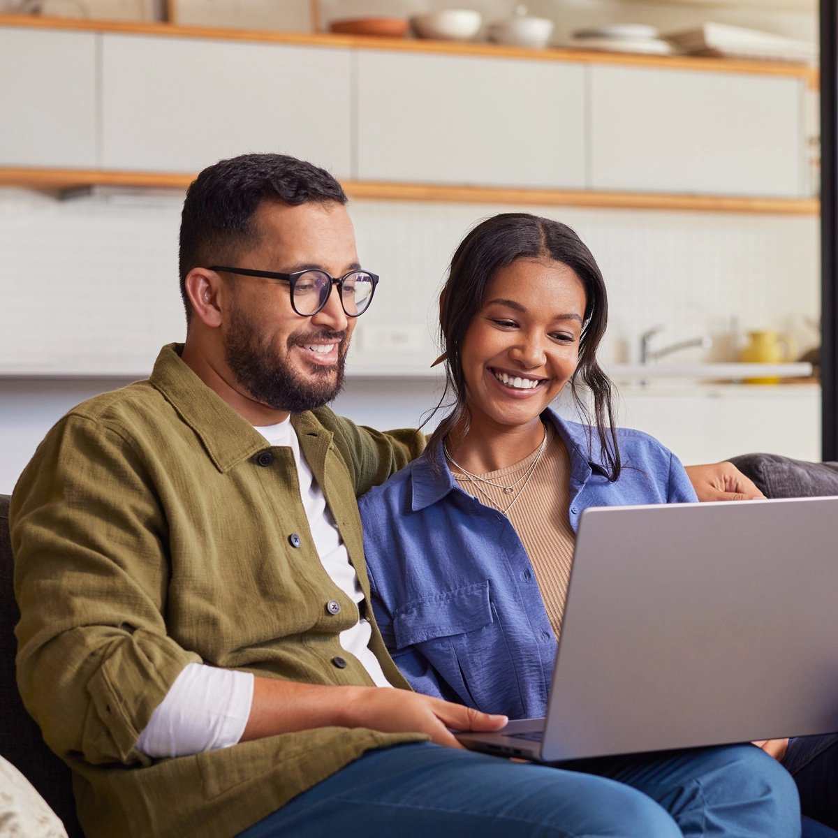 Couple sitting at home looking at houses on the computer together.